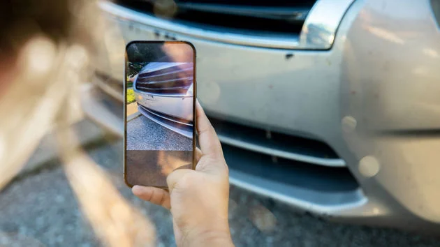 Hand holding a phone showing a damaged car